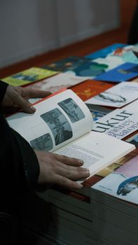 A person browsing through various books at an indoor market stall, viewing photographs.