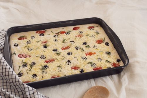 Free Unbaked focaccia dough topped with cheese, olives, tomatoes, and rosemary. Stock Photo
