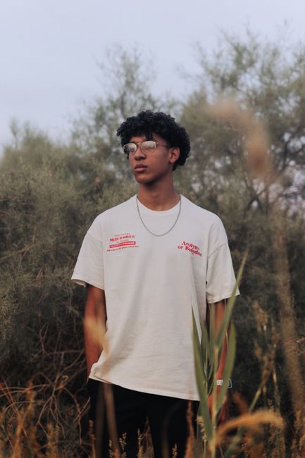 A young man with glasses standing in a grassy field, captured outdoors in natural light.