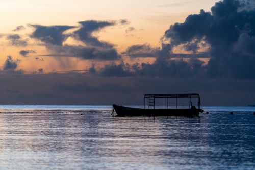Free Silhouette of a lone boat floating on the sea with an enchanting sunset and dramatic clouds in the background. Stock Photo