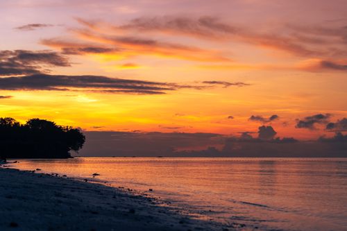 Free Tranquil sunrise over a peaceful beach with vibrant orange and purple hues creating a dramatic sky. Stock Photo