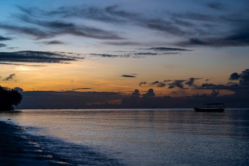 Free A tranquil beach sunset with a silhouetted boat on calm waters, perfect for serene landscapes. Stock Photo