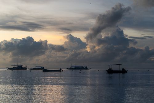 Free Silhouetted boats on calm water with a dramatic cloudscape during sunset. Stock Photo
