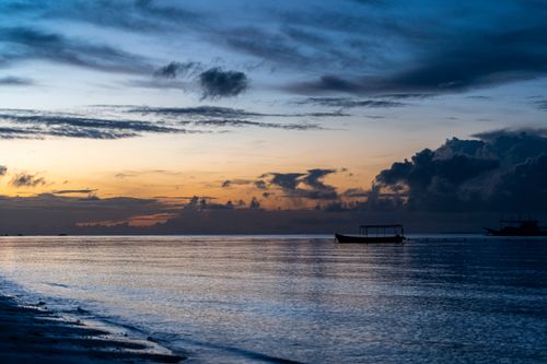 Free A serene sunset over a calm sea with a silhouetted boat, perfect for peaceful and contemplative themes. Stock Photo