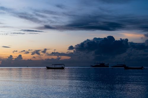 Free Serene seascape with boats silhouetted against a dramatic sunset sky. Stock Photo