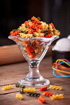 Vibrant tri-color fusilli pasta elegantly displayed in a glass bowl on a wooden table.