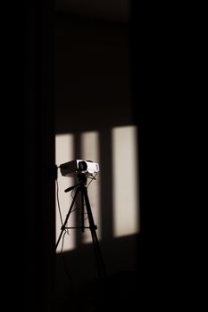 A vintage projector on a tripod casting shadows in a dimly lit room, creating a mysterious atmosphere.