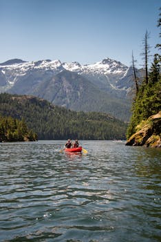 一艘红色独木舟在宁静的湖面上划行，四周环绕着雄伟的山峰