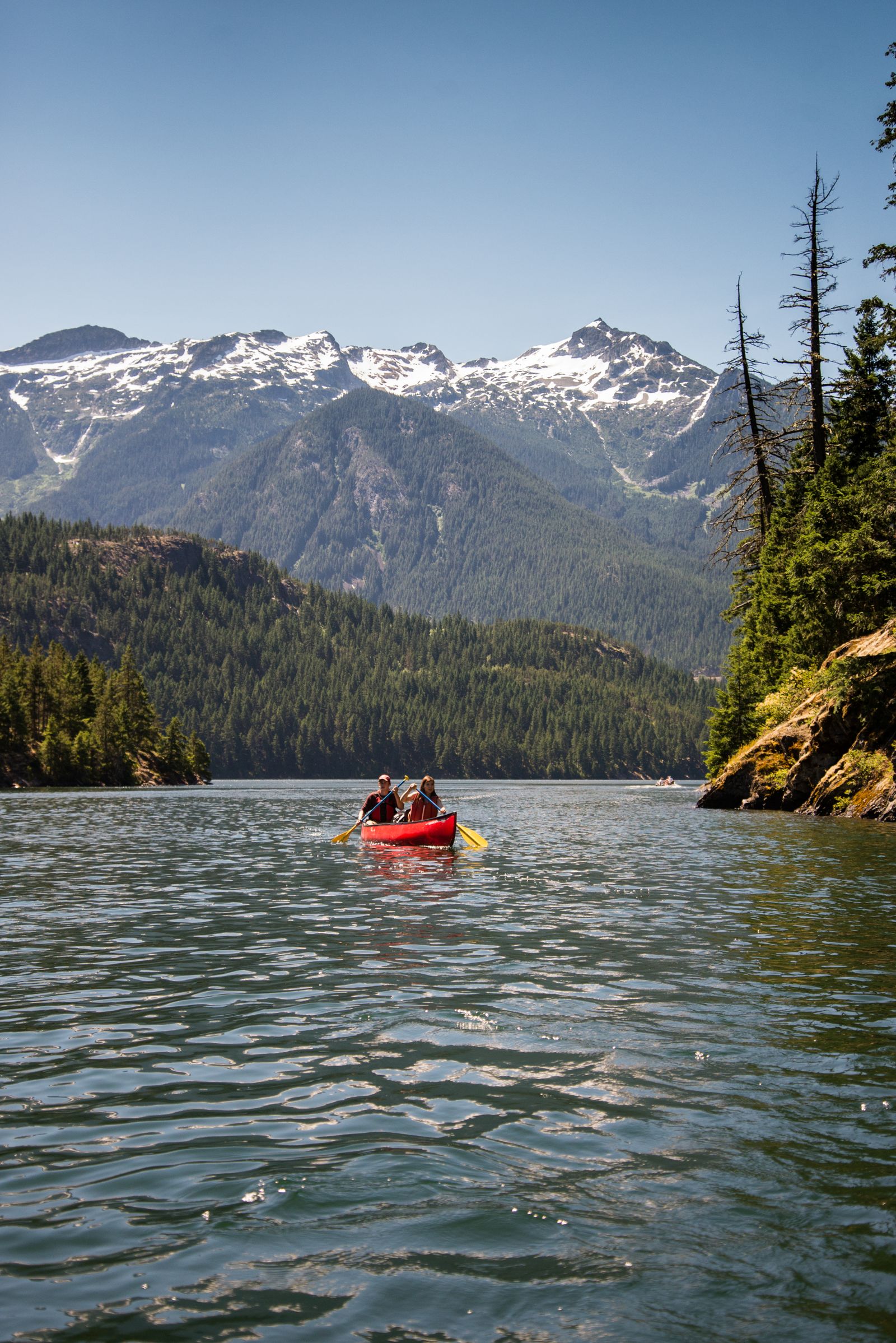 A vivid red canoe on a bright blue lake surrounded by green forest and mountains