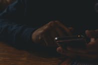 昏暗室内，双手操作智能手机的特写镜头，凸显了技术的运用