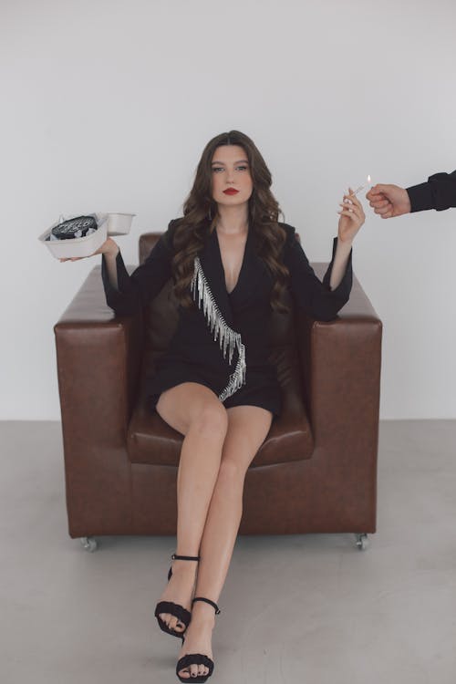 Young Woman Sitting in an Armchair with a Cake and One Hand and Cigarette in the Other 