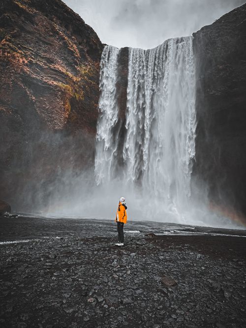 Free A person stands in awe before the majestic Skogafoss in Iceland, surrounded by nature's beauty. Stock Photo