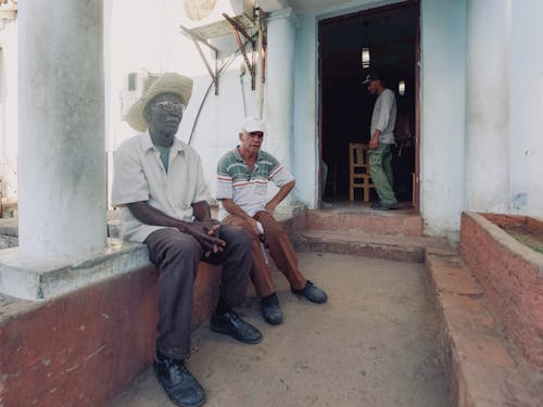 Men in Cap and Hat Sitting on Wall