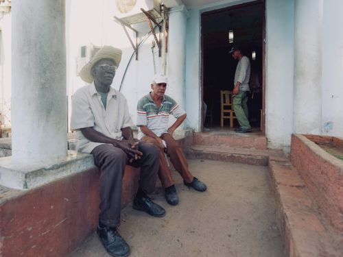 Free Three men seated and standing by a doorway of a house, engaging in conversation. Stock Photo