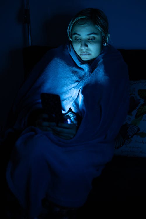 Woman Sitting with Smartphone in Darkness