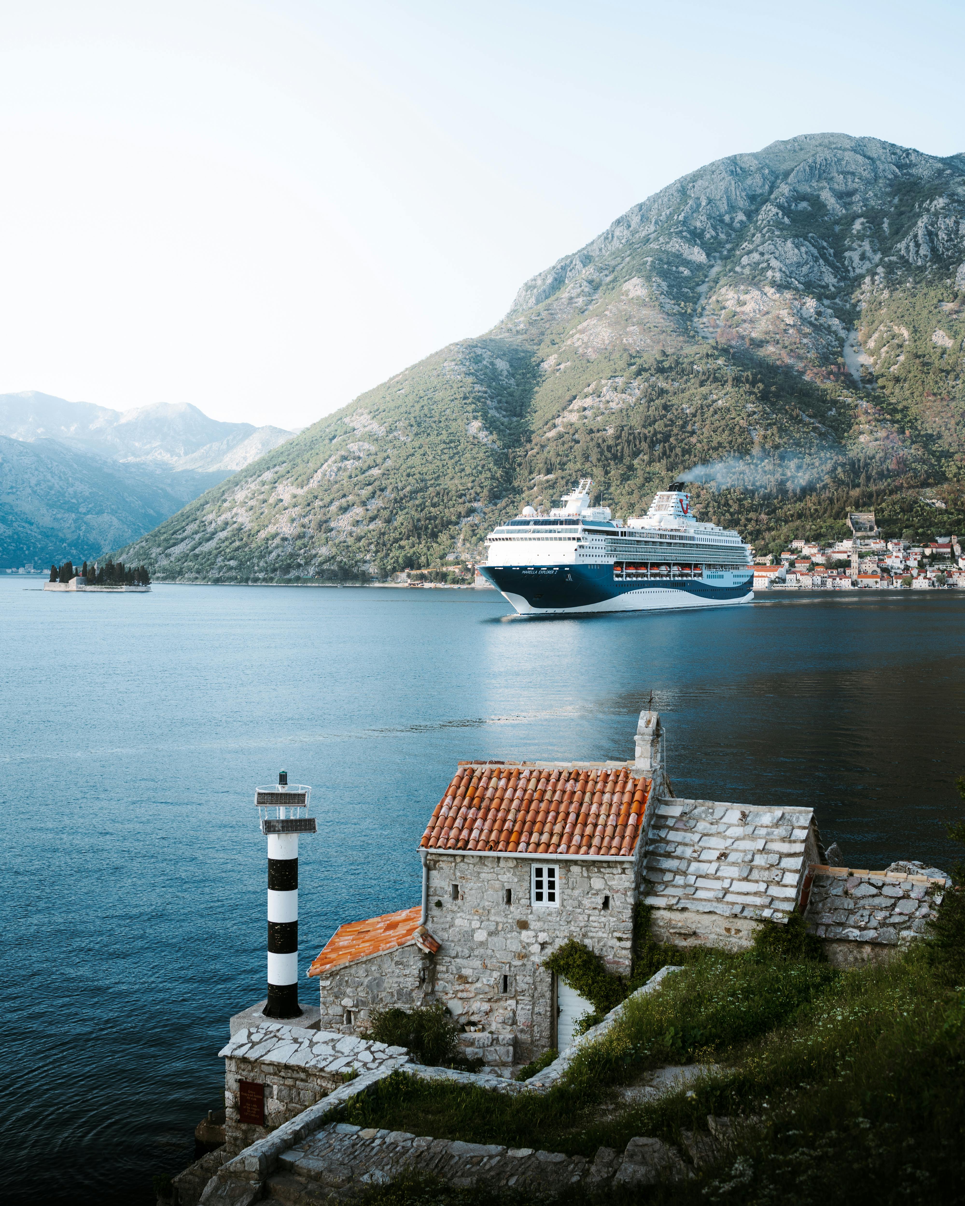 Cruise ship traversing Kotor Bay with scenic coastal architecture and hills.