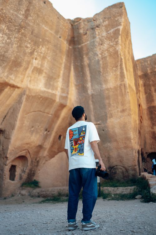 Free Man in white t-shirt observing towering eroded rock formation outdoors. Stock Photo