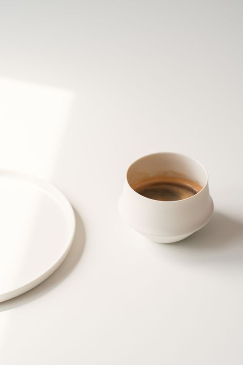 Free A minimalist coffee cup on a white background, captured in a soft, warm light. Stock Photo