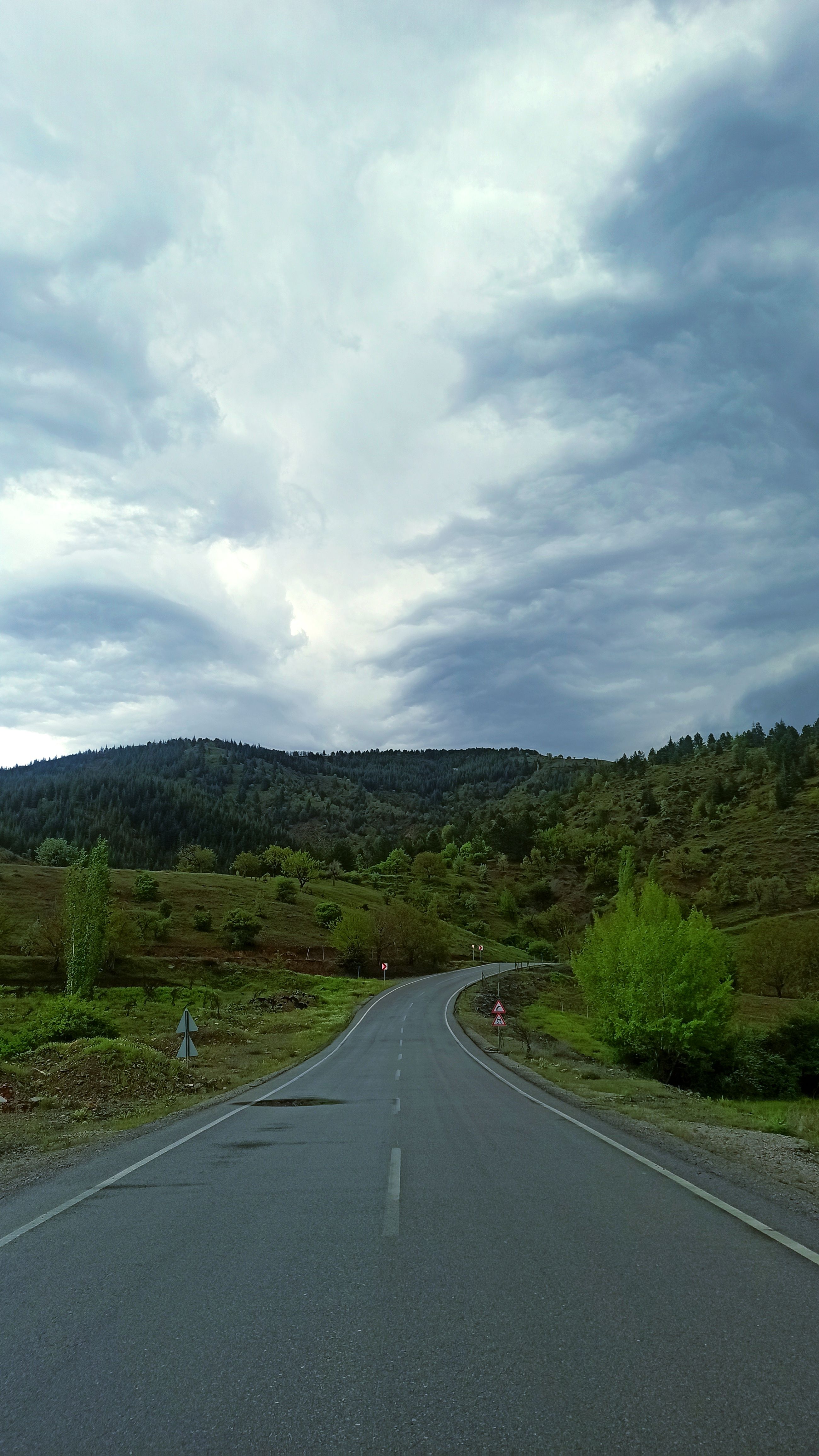 A winding road leads through lush green hills under an overcast sky, creating a picturesque scene.