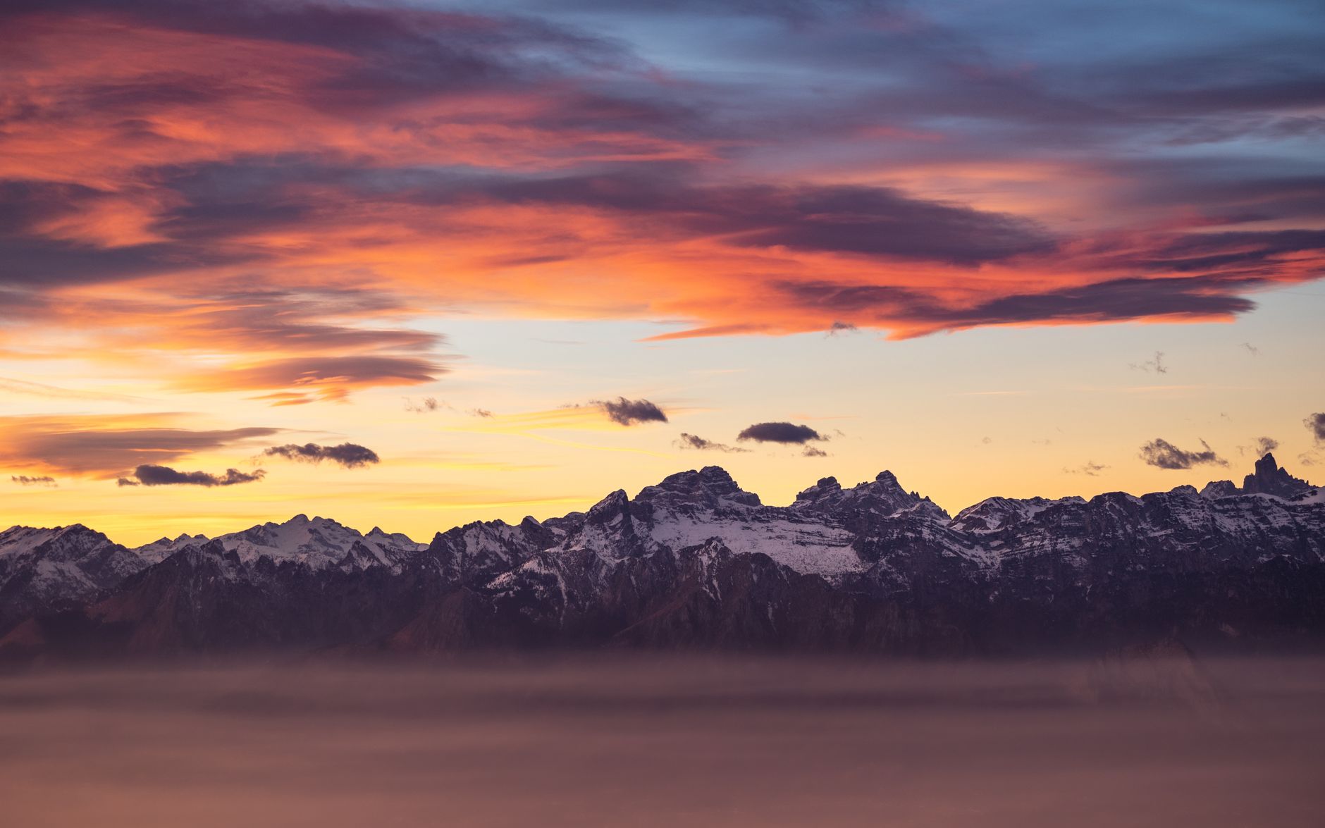 Breathtaking view of the Alpine mountains with dramatic sunset skies and snowy peaks.