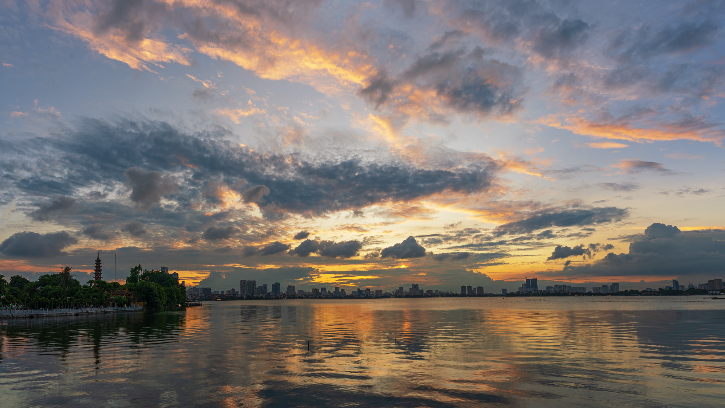 Stunning sunset view over West Lake with Hanoi skyline reflection.