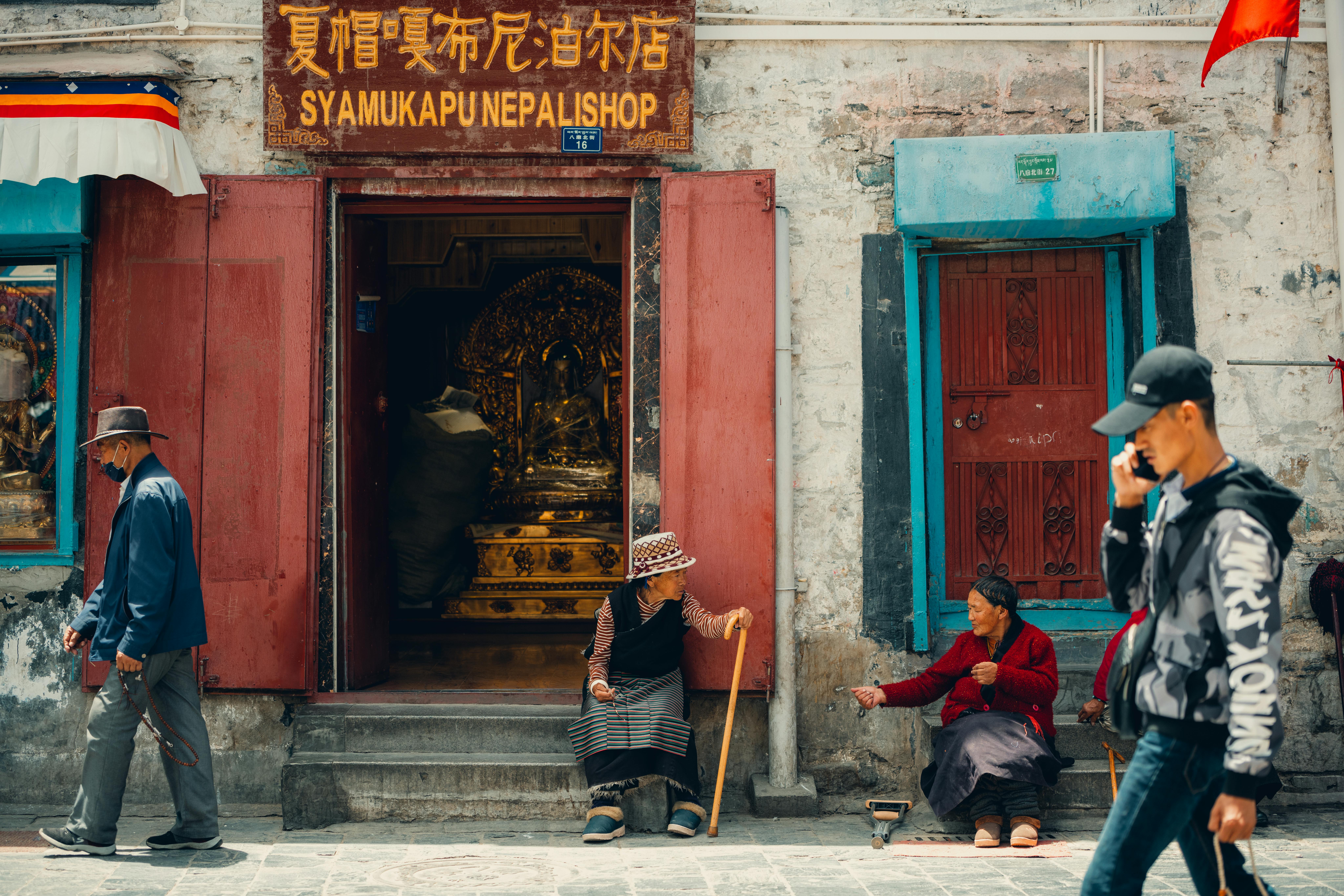 man talking on phone passing two women sitting in front of building