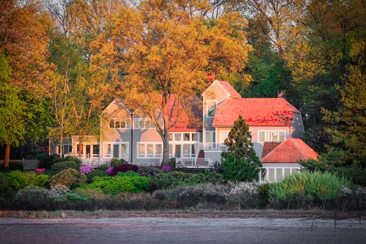 Beautiful home with red roof nestled among vibrant autumn foliage and lush garden.