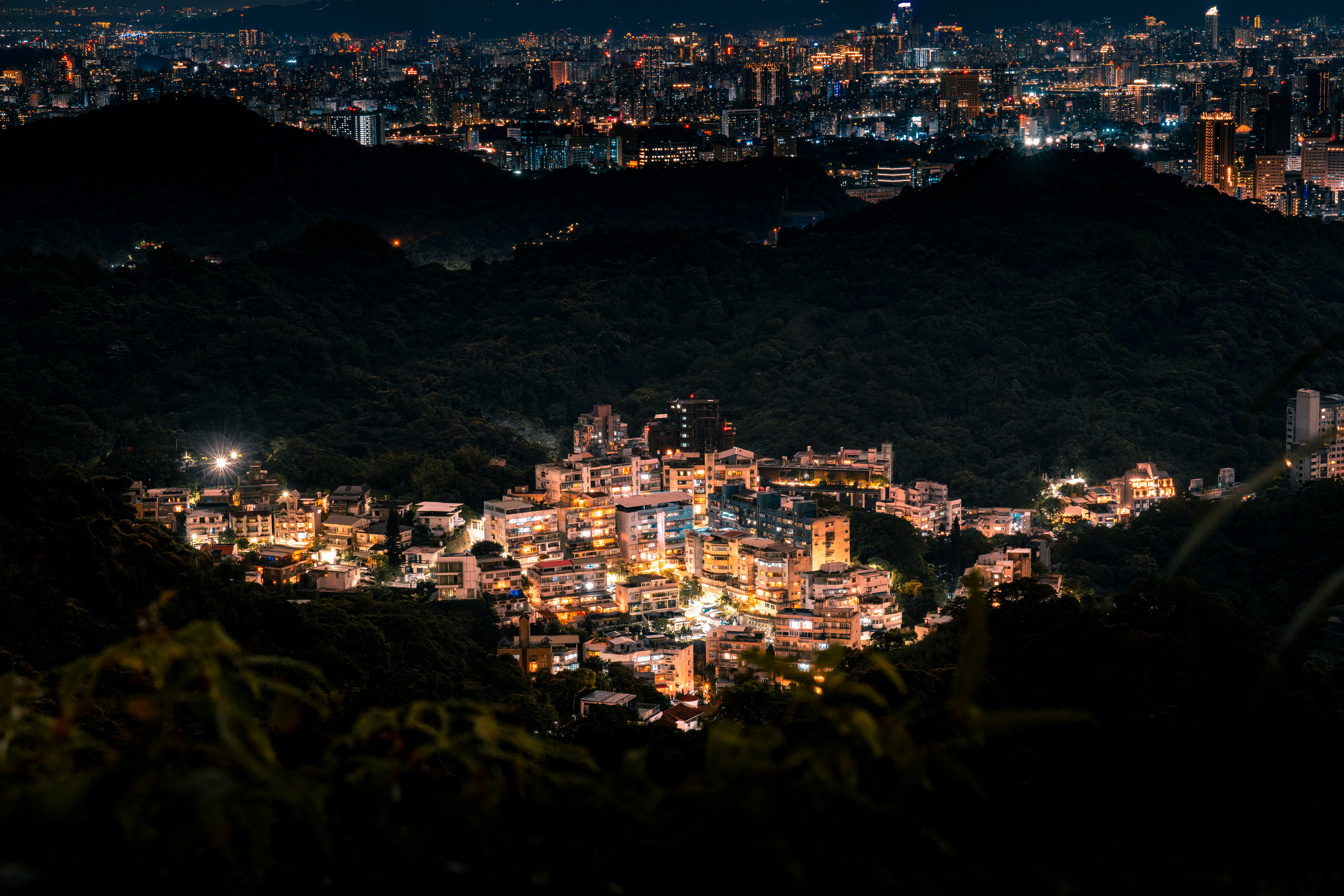A captivating aerial view of Taipei cityscape and illuminated urban area at night, surrounded by lush hills.