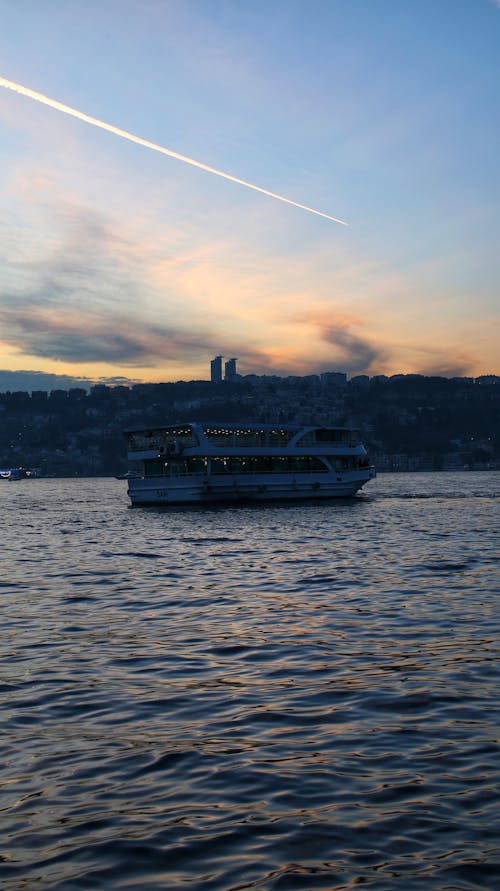 A Passenger Boat Sailing in the Bay with the View of City in the Background at Sunset 