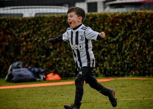 A young boy enthusiastically playing soccer in sportswear during a rainy day training session.