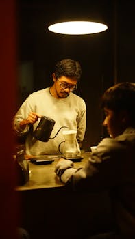 A barista carefully pours coffee while another person observes at a cozy café.
