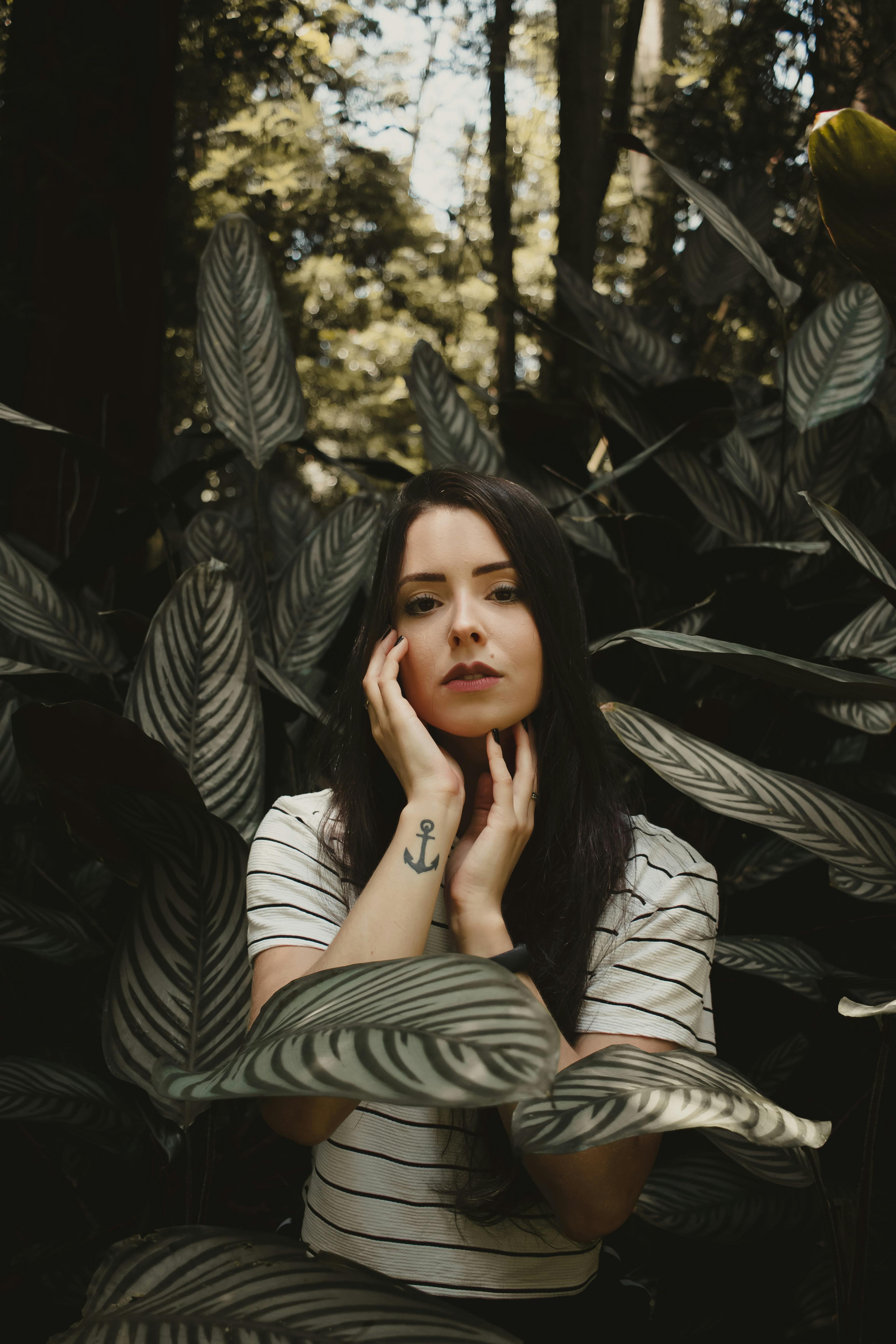 Caucasian woman with anchor tattoo in lush forest setting.