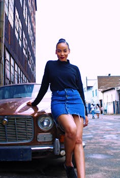 一位身穿牛仔裙的自信女性在城市户外环境中，在一辆老爷车旁摆姿势