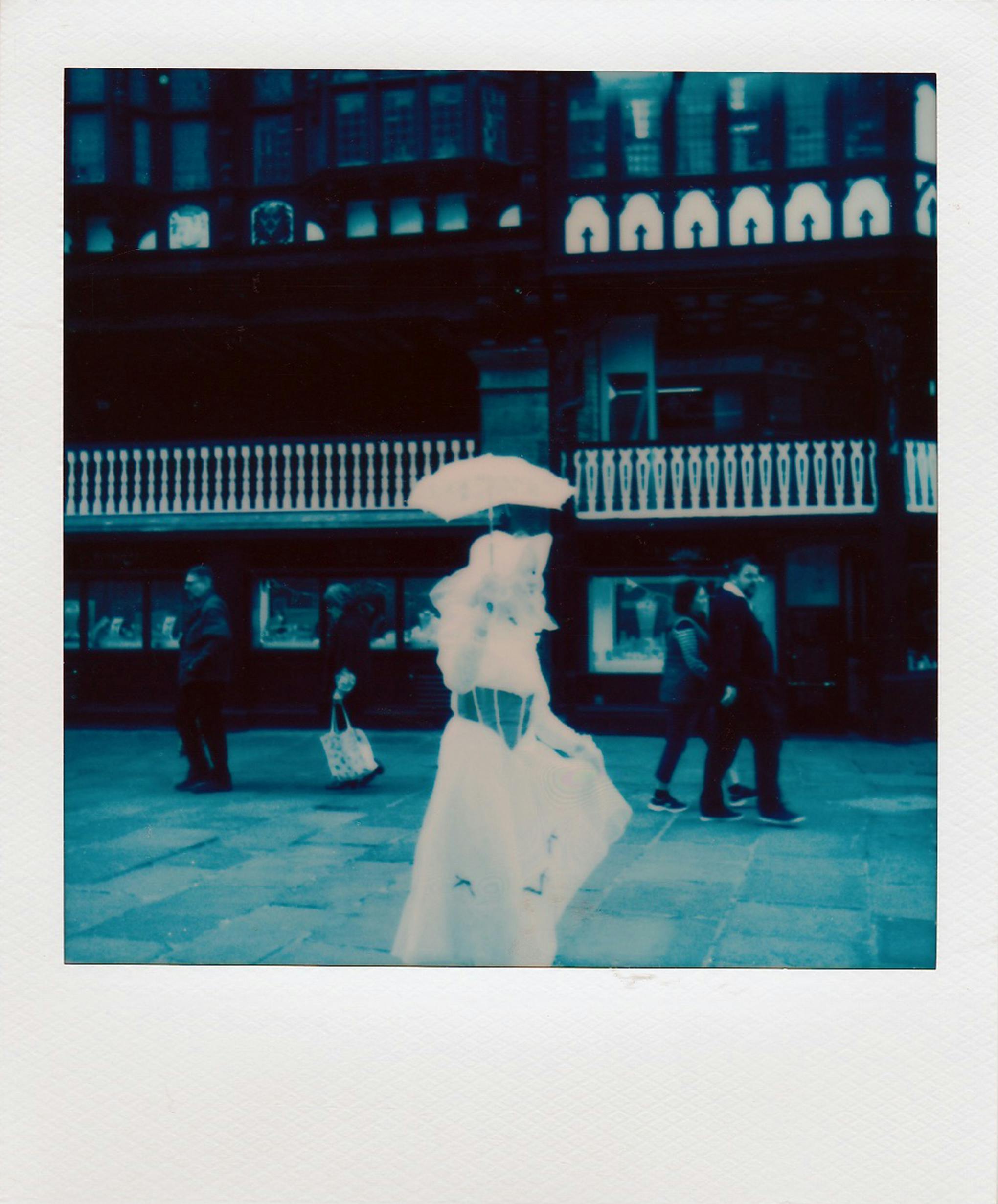 Stylized vintage photo of a woman with an umbrella on a bustling street.