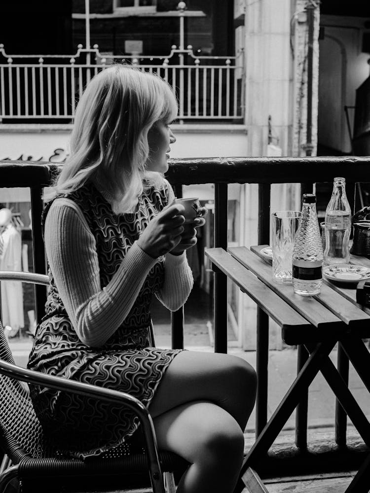 Woman Sitting At Cafe Table Drinking Coffee