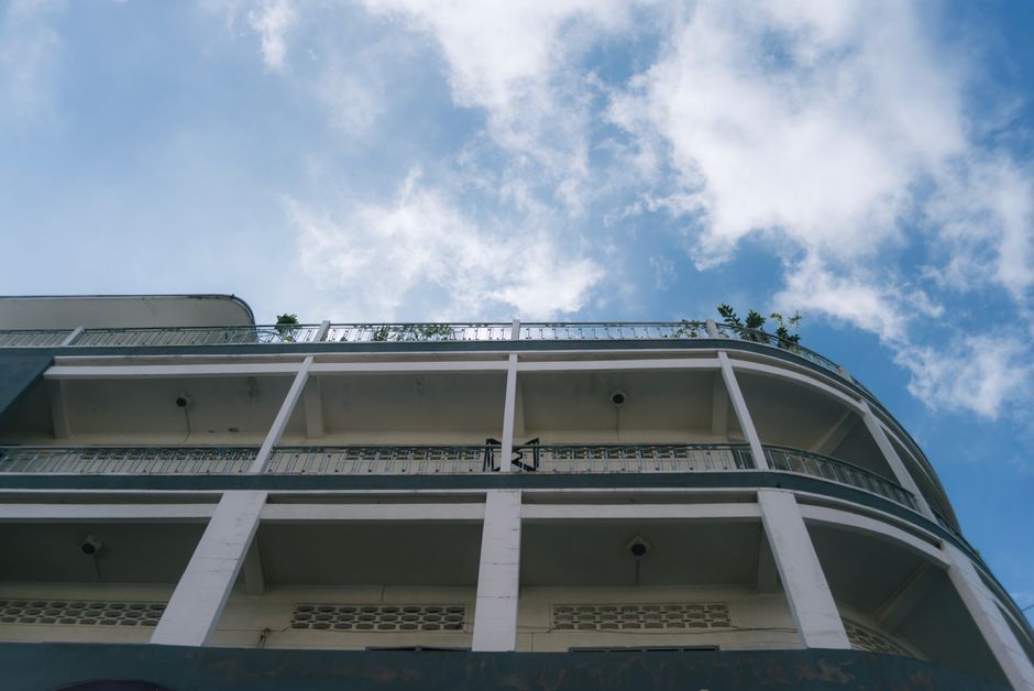 Low-angle view of a multi-storey building exterior with tiered balconies against a blue Mediterranean sky.