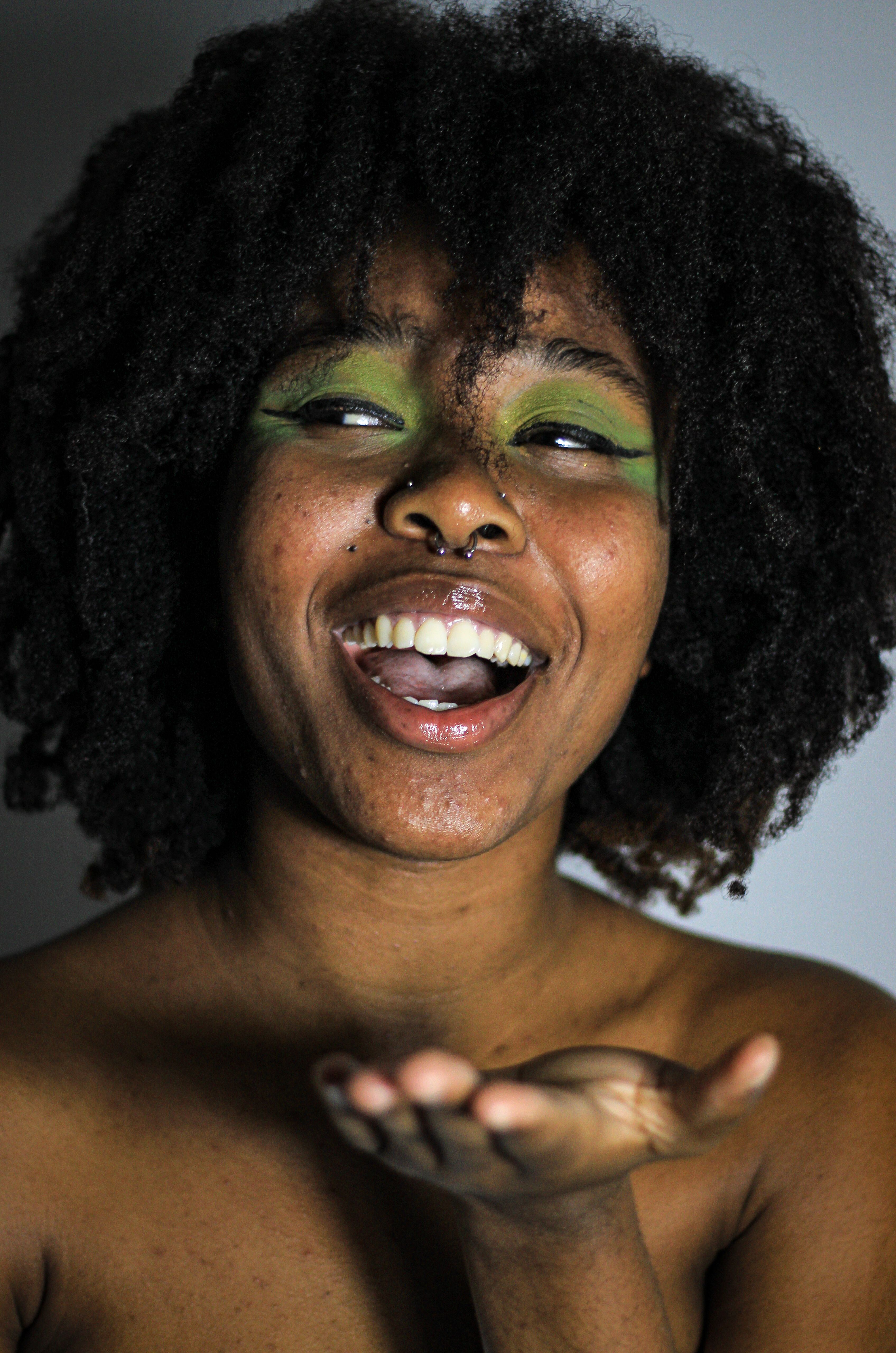 Cheerful African woman with afro hairstyle and green eye makeup, smiling in a studio setting.