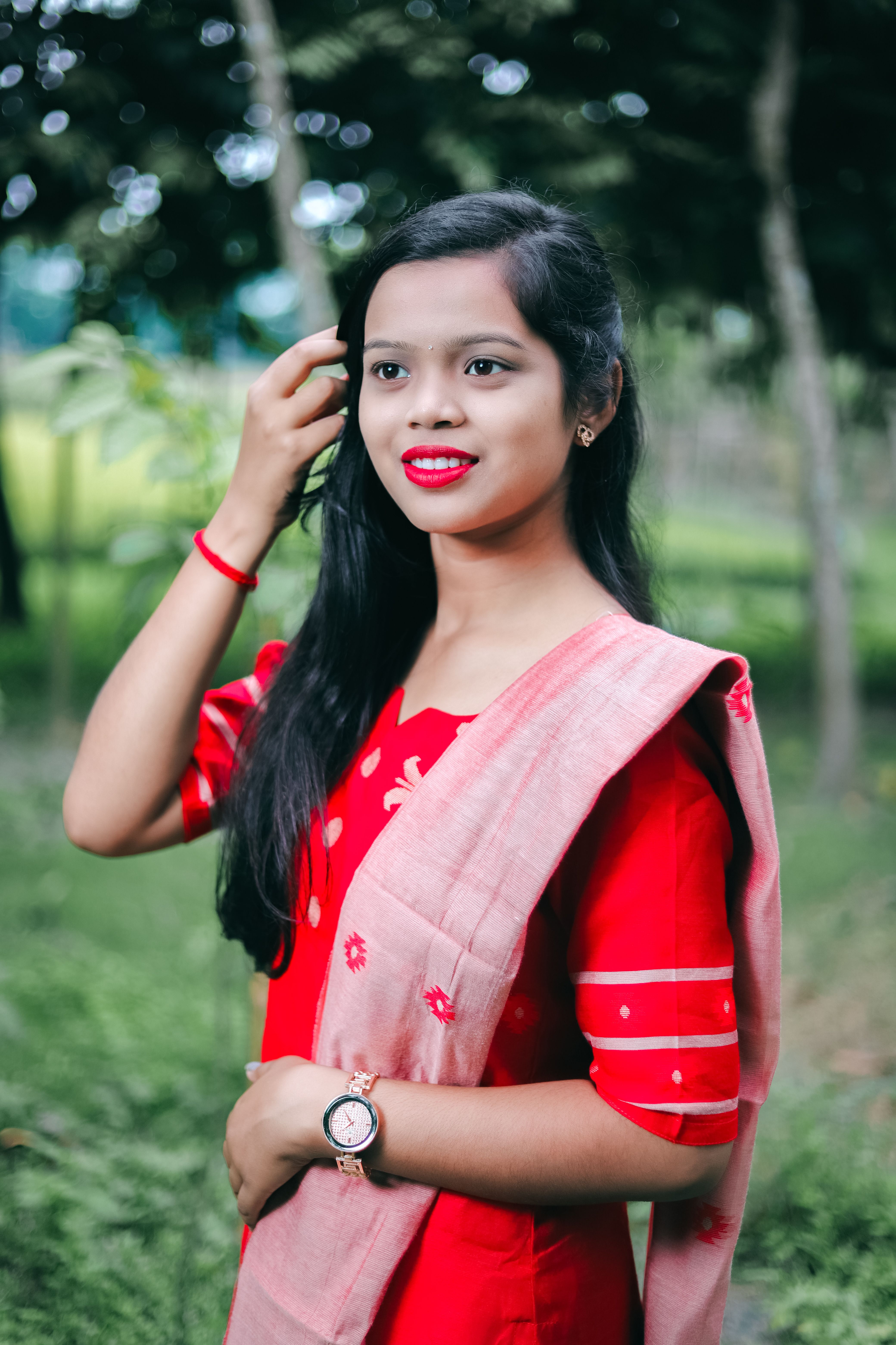 Young woman in traditional red attire posing gracefully in a lush green park in Dhaka, Bangladesh.