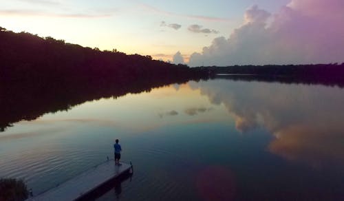 Mann, Der Auf Flussdock Während Des Sonnenuntergangs Steht
