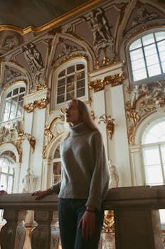 在一座装饰华丽、内有雕塑和镀金细节的建筑里，一位穿着毛衣的女人站着