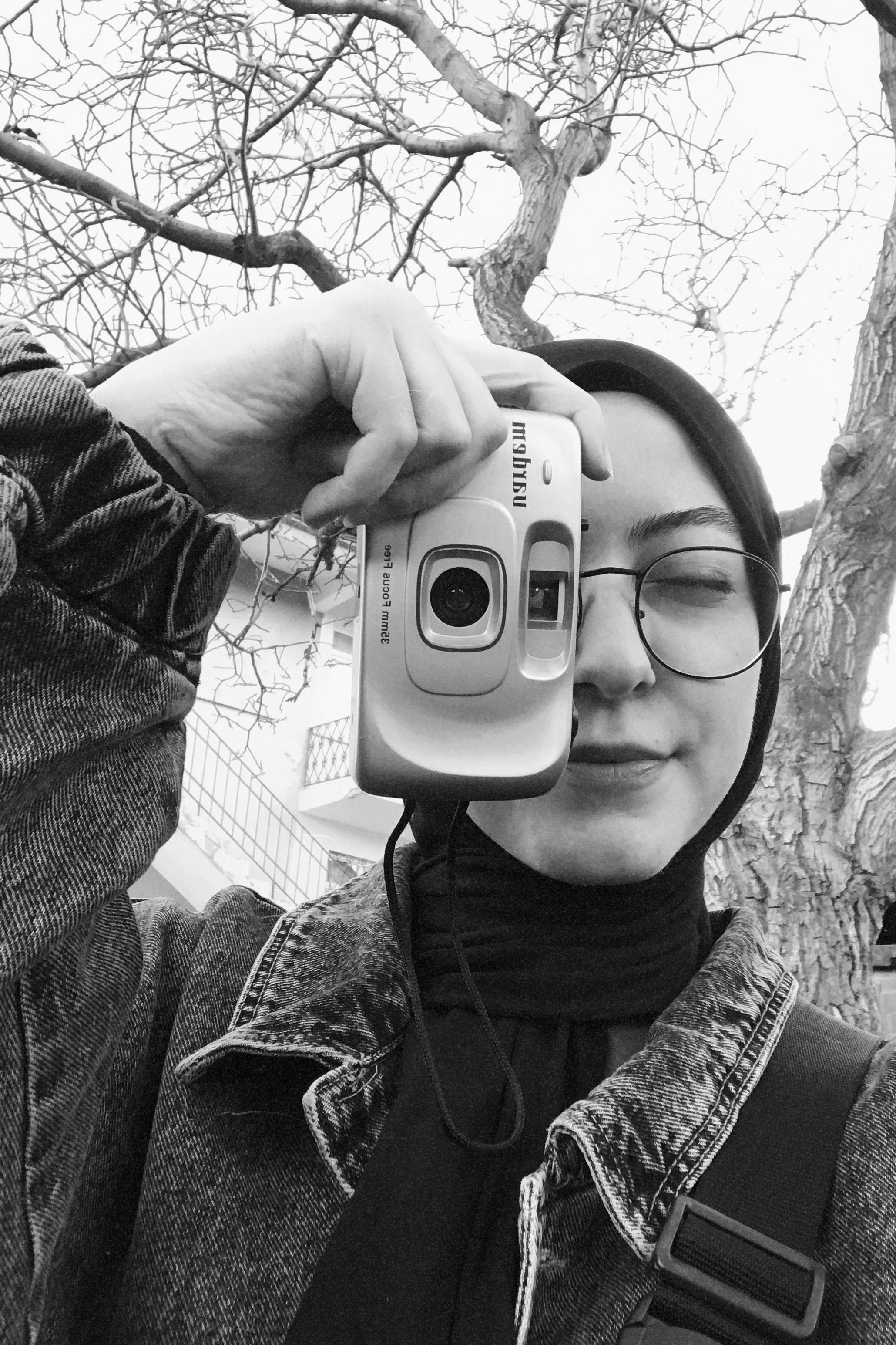 Black and white photo of a woman in hijab using a point-and-shoot camera