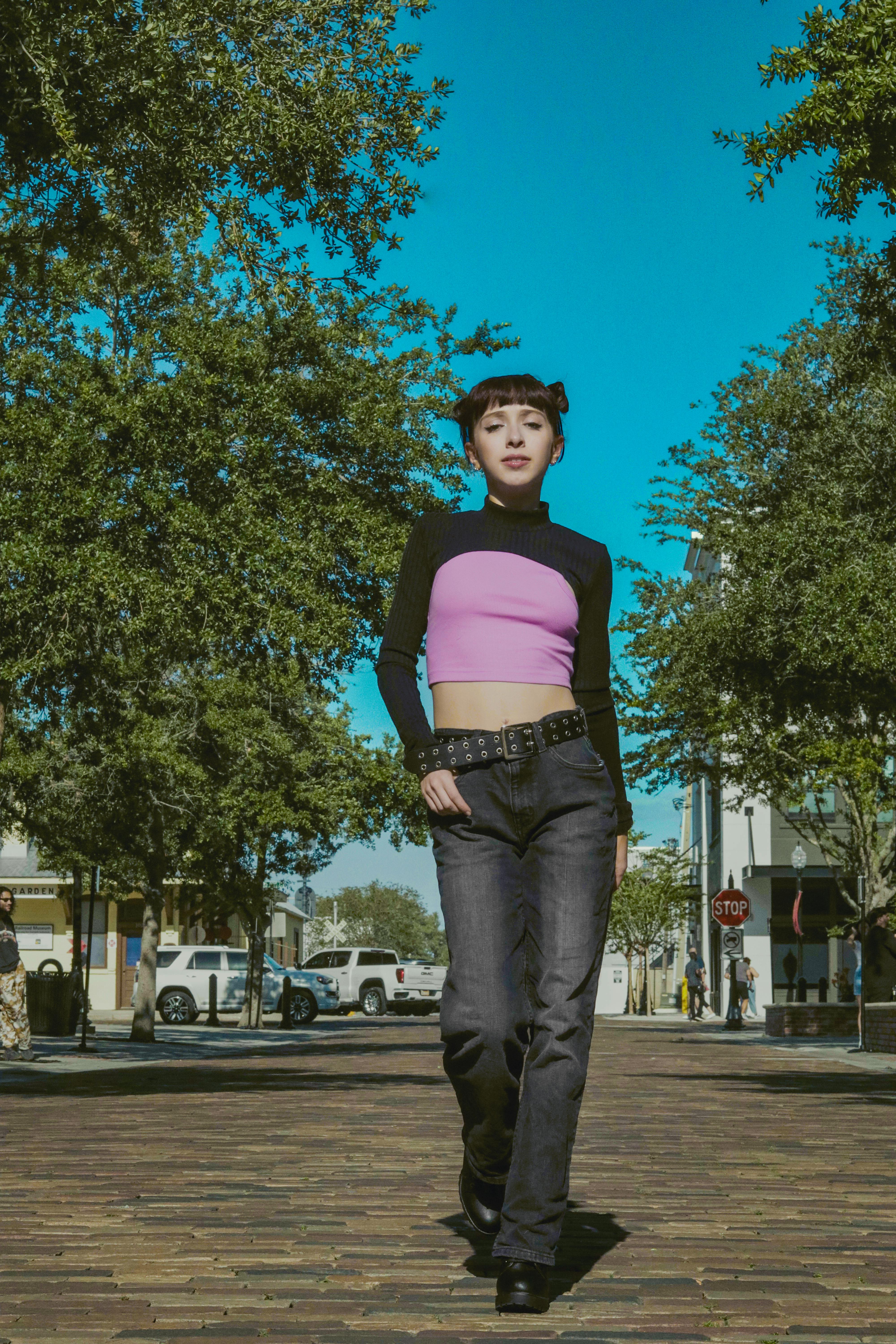 Young woman in stylish outfit walking through a sunlit urban alley.