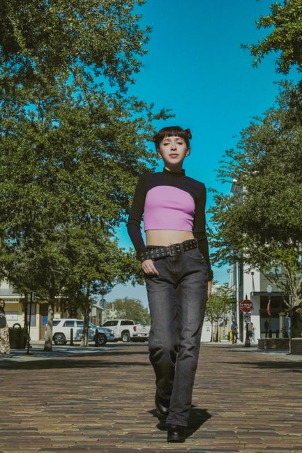 Young woman in stylish outfit walking through a sunlit urban alley.
