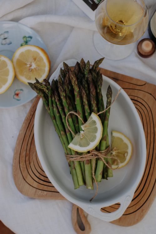 Free A vibrant bundle of fresh asparagus with lemon slices on a white serving plate, perfect for a healthy meal. Stock Photo