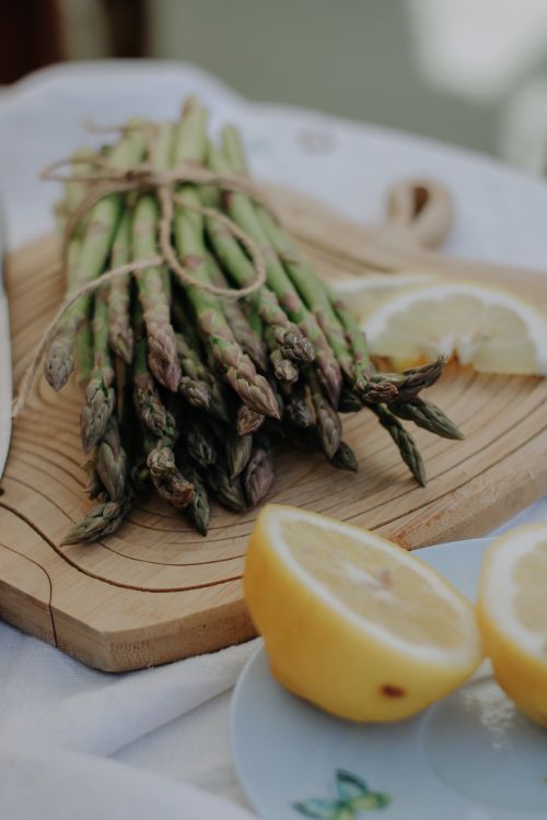 Free A bunch of fresh asparagus tied with string, accompanied by sliced lemons on a wooden board. Stock Photo