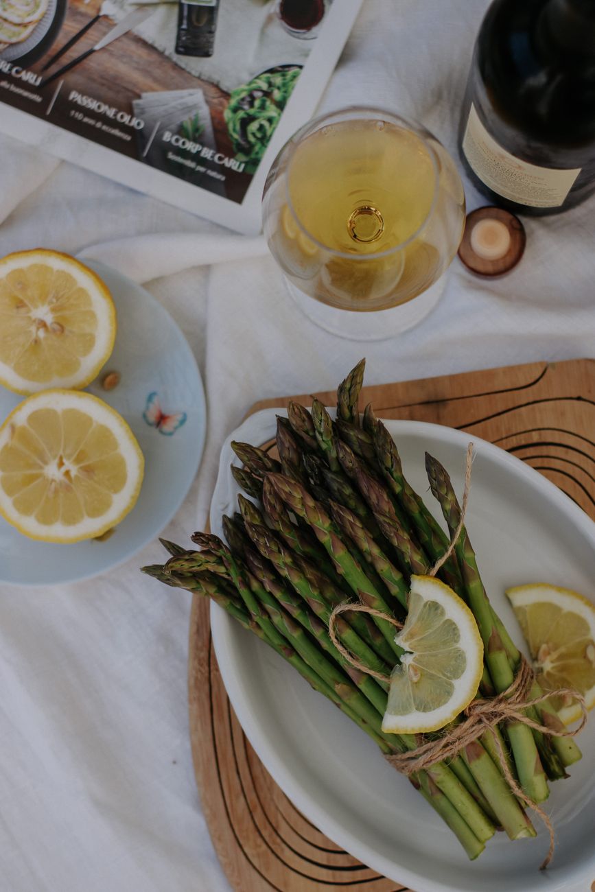 Top view of asparagus bundle with lemon slices and white wine on a table setting.