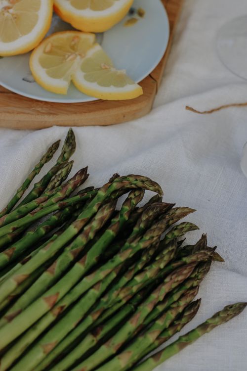 Free A bundle of fresh asparagus next to lemon slices on a white tablecloth. Stock Photo