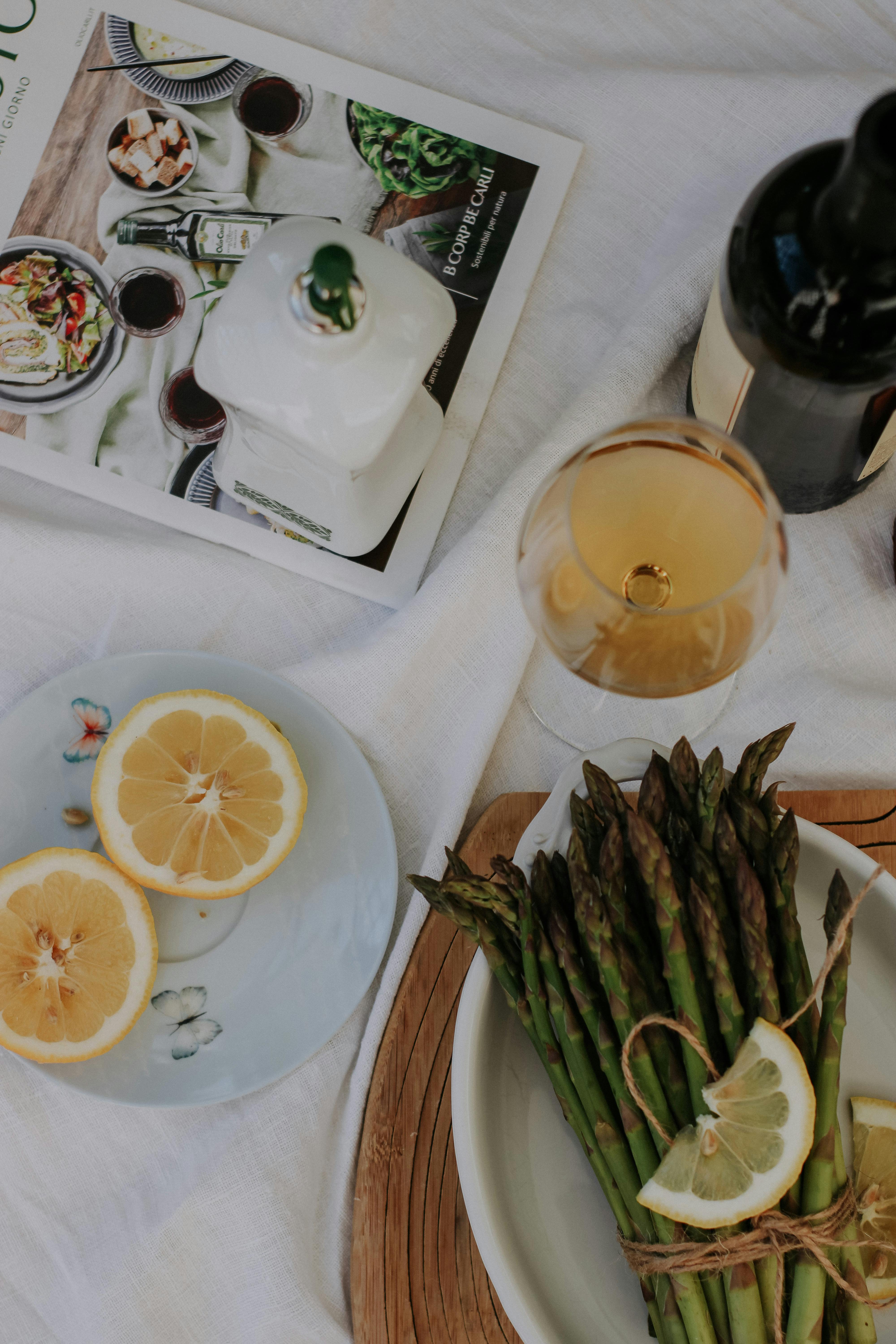 A sophisticated arrangement of asparagus, lemon slices, and a glass of white wine on a rustic table setting.
