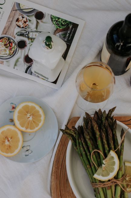 A sophisticated arrangement of asparagus, lemon slices, and a glass of white wine on a rustic table setting.