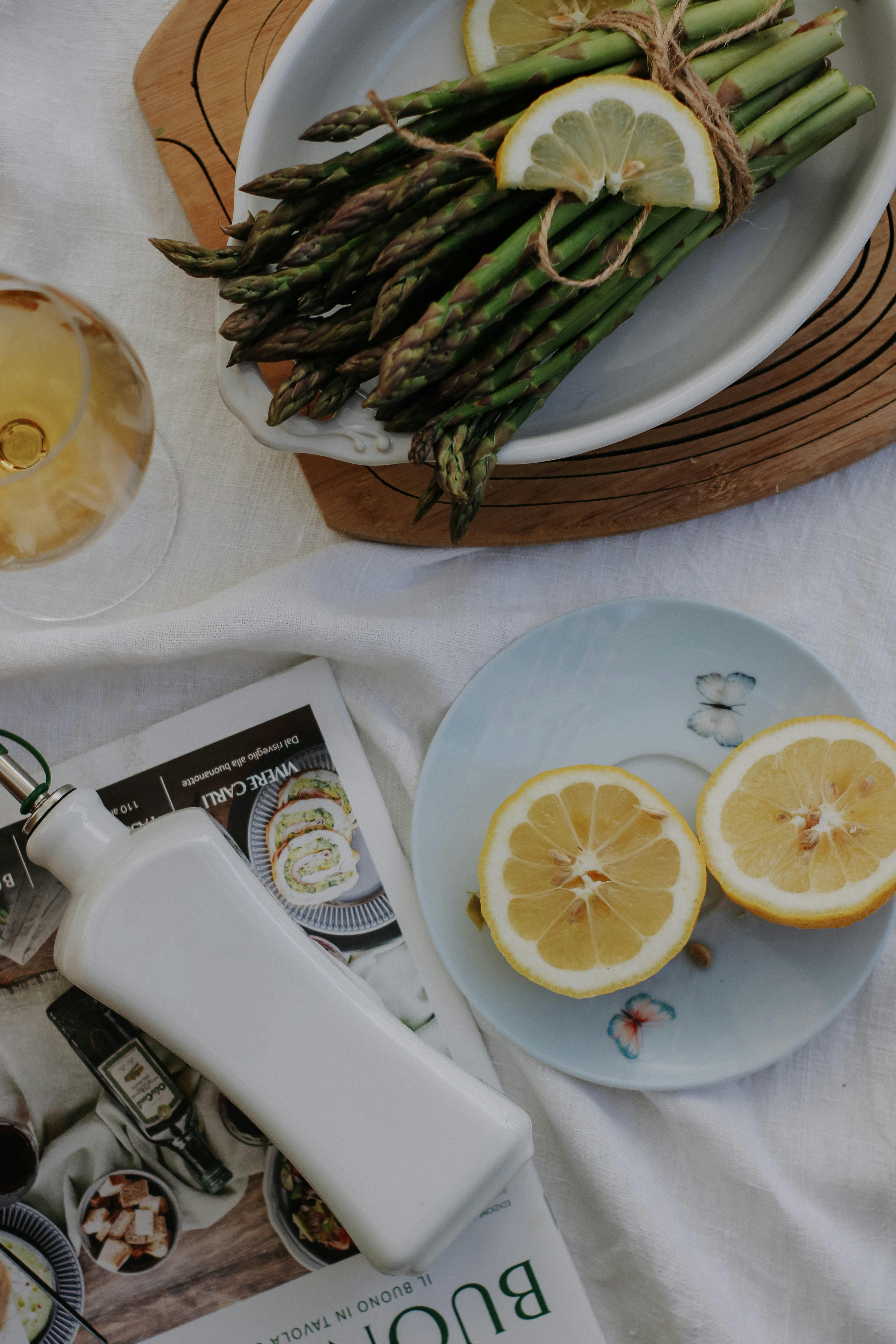 A stylish food setup featuring asparagus, lemon slices, and white wine on a table.
